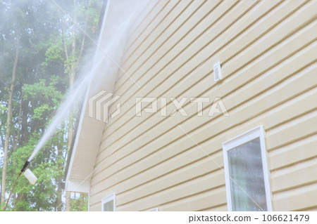 Using high pressure nozzles, service worker efficiently washes siding houses with water soap cleaner 106621479