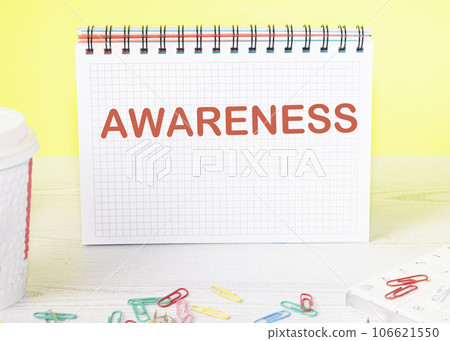 AWARENESS the word is written on a blank sheet in a notebook standing on a table on a yellow background 106621550