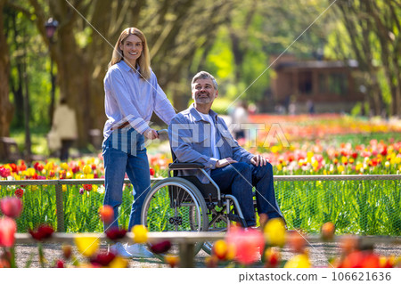 Middle aged wife and disabled husband in wheelchair walking in park. 106621636
