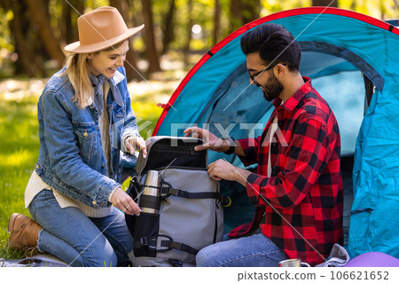 Two young people sitting at the tent in the forest and looking excited Two young people sitting at the tent in the forest and looking excited 106621652
