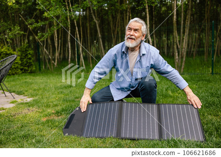 Mature man holding solar panel in garden. Mature man holding solar panel in garden. 106621686