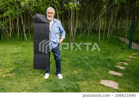 Senior man holding solar panel on in green yard. 106621690