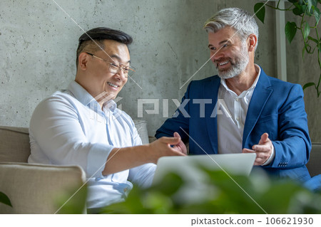 Business men sitting on sofa in modern office talking together and using laptop. 106621930