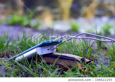 Portable charger charges a smartphone in nature. Power Bank on a journey to charge gadgets. 106622205