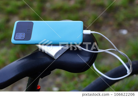 A portable charger charges a smartphone on the background of a bicycle and nature. Power Bank on a journey to charge gadgets. 106622206