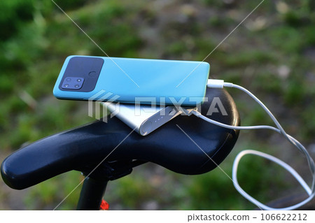 A portable charger charges a smartphone on the background of a bicycle and nature. Power Bank on a journey to charge gadgets. 106622212