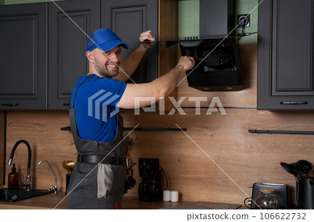 A handyman in uniform, installs or repairs a kitchen hood, replaces the filter in the hood. Construction, maintenance and repair concept 106622732