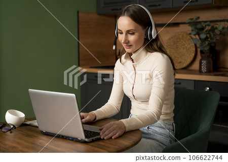 Woman is sitting in the kitchen, communicating via video call via laptop with a friend, sitting at a table in the kitchen of her house 106622744