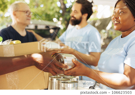 Multiethnic volunteers in a charitable event, handing out food to the poor and needy. Smiles abound as voluntary individuals work together to fight hunger and provide support to the less fortunate. Multiethnic volunteers in a charitable event, handing out food to the poor and needy. Smiles abound as voluntary individuals work together to fight hunger and provide support to the less fortunate. 106623503