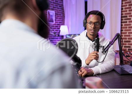 Podcast presenter having live discussion with man, streaming it online for audiences watching show. Influencer enjoying chat with guest, broadcasting in home studio living room with rgb lights Podcast presenter having live discussion with man, streaming it online for audiences watching show. Influencer enjoying chat with guest, broadcasting in home studio living room with rgb lights 106623515
