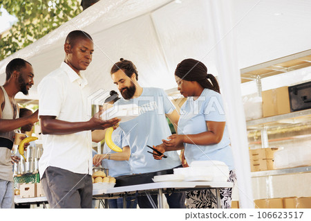 Diverse volunteers collaborate at homeless center, distributing essentials, serving free food to underprivileged, supporting hunger relief. Group of voluntary people provide aid to the poor and needy. 106623517