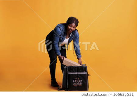 African american employee holding cardboard full with pizza ready to deliver to customer during lunch time in studio with yellow background. Pizzeria courier delivering takeaway food meal African american employee holding cardboard full with pizza ready to deliver to customer during lunch time in studio with yellow background. Pizzeria courier delivering takeaway food meal 106623531