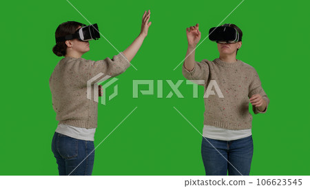 Close up of modern person having fun with vr glasses on greenscreen backdrop, using virtual reality headset with artificial intelligence. Woman enjoying interactive 3d goggles in studio. 106623545