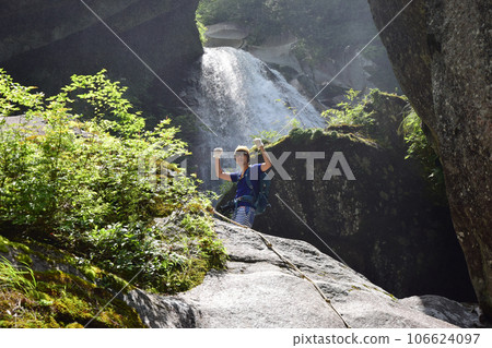 A man with glasses doing a guts pose in front of a waterfall 106624097