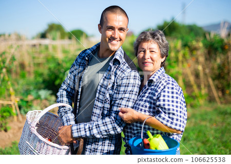 Smiling man and his elderly mother standing with garden tools outdoors 106625538