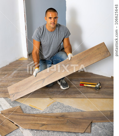 Portrait of concentrated young man in ordinary clothes installing new wooden laminate flooring Portrait of concentrated young man in ordinary clothes installing new wooden laminate flooring 106625648