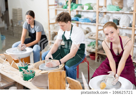 Pottery master together with students create pottery on a potter's wheel in workshop 106625721