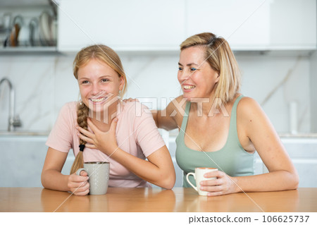 Cheerful woman with teenage daughter talking over coffee at home Cheerful woman with teenage daughter talking over coffee at home 106625737