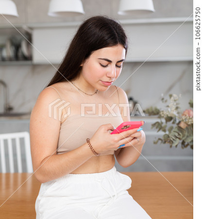 Young woman reading message on phone in kitchen Young woman reading message on phone in kitchen 106625750