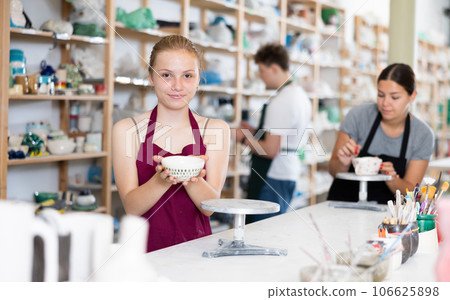 Teenage girl posing with ceramic cup in ceramic workshop 106625898