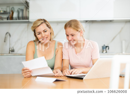 Cheerful woman with teenage daughter reading letter together Cheerful woman with teenage daughter reading letter together 106626008