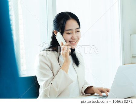 年輕女子在電腦前用智能手機交談 106628271