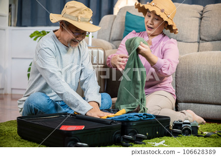 Asian romantic retired couple packing clothes travel bag suitcase together on floor at home interior living room, couple old senior married retired prepare luggage suitcase arranging for travel Asian romantic retired couple packing clothes travel bag suitcase together on floor at home interior living room, couple old senior married retired prepare luggage suitcase arranging for travel 106628389