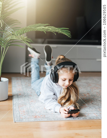 Little girl listening music lying on the floor Little girl listening music lying on the floor 106629505