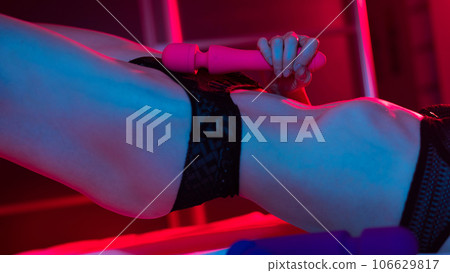 A faceless woman lies in a bedroom in a blue-red neon light and uses a pink vibrator. Close-up of the abdomen. A faceless woman lies in a bedroom in a blue-red neon light and uses a pink vibrator. Close-up of the abdomen. 106629817