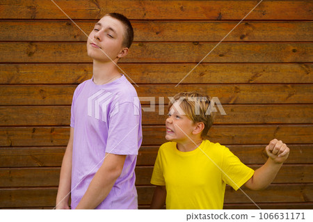 Brothers Conflicts. Offended brothers standing Back To Back Not Talking To Each Other, wooden wall with copy space. Rivalry concept 106631171