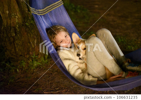 Cute little girl child sleeping in hammock and holding a corgi dog together in camping trip Cute little girl child sleeping in hammock and holding a corgi dog together in camping trip 106631235