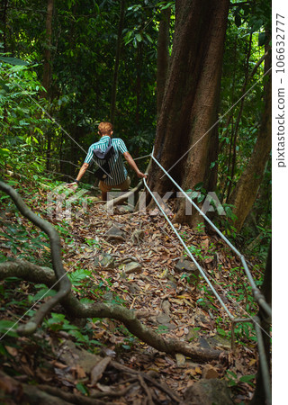 Man hikes in mountainous tropical forest holding security ropes. Visiting Khao Phanom Bencha National Park in Krabi, Thailand 106632777