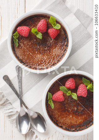Chocolate creme brulee with caramel crust garnished with mint and raspberries close-up in ramekin. Vertical top view 106633410