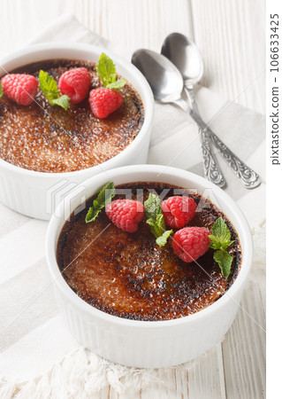 Chocolate creme brulee with caramel crust garnished with mint and raspberries close-up in ramekin. Vertical 106633425