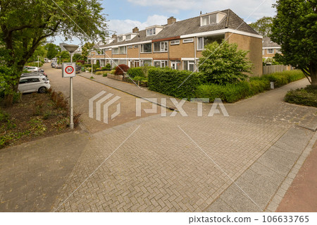 a street with houses in the background and trees on either side, some cars are parked near each other buildings 106633765
