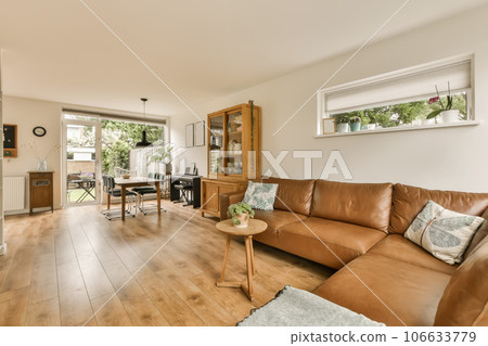 a living room with wood flooring and brown leather couches in the center of the room is an open kitchen, dining area 106633779