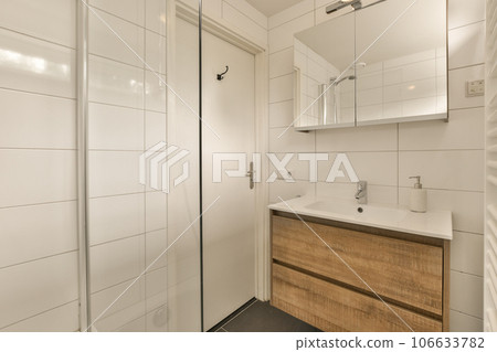 a bathroom with white tiles on the walls and wood cabinetd vanity in the corner, next to a glass shower door a bathroom with white tiles on the walls and wood cabinetd vanity in the corner, next to a glass shower door 106633782