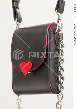 Small elegant black bag with red inserts in the shape of a heart and a silver chain, close-up 106633961