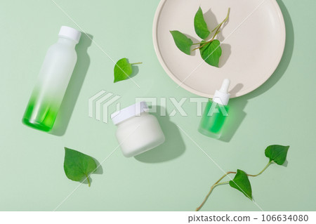 Top view of cosmetic bottle unlabeled mockup for design, decorated with fish mint leaves and ceramic dish on pastel green background. Fish mint has several healing qualities. 106634080