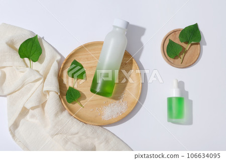 A glass bottle unlabeled on wooden plate decorated with fish mint leaves and cotton towel on a white background. Space for design, advertising and branding cosmetic product A glass bottle unlabeled on wooden plate decorated with fish mint leaves and cotton towel on a white background. Space for design, advertising and branding cosmetic product 106634095