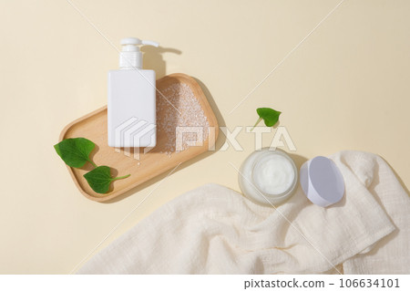 Top view of a pump bottle and a white cream jar unlabeled displayed on a beige background with fresh fish mint leaves and bath salt. Mockup scene for advertising cosmetic of fish mint extract Top view of a pump bottle and a white cream jar unlabeled displayed on a beige background with fresh fish mint leaves and bath salt. Mockup scene for advertising cosmetic of fish mint extract 106634101