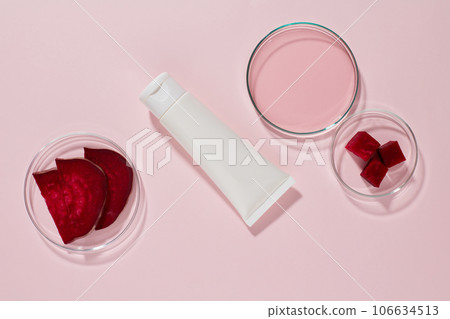 A white plastic tube unbranded displayed on a pink background with petri dishes containing slices and essence of beetroot. Mockup for design, advertising and branding cosmetic extracted from beetroot A white plastic tube unbranded displayed on a pink background with petri dishes containing slices and essence of beetroot. Mockup for design, advertising and branding cosmetic extracted from beetroot 106634513