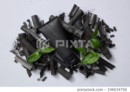 A black tube of facial cleanser with bamboo charcoal and tea leaves on gray background. Bamboo charcoal and green tea are a duo of cleansing active ingredients that are widely used in facial cleansers 106634798