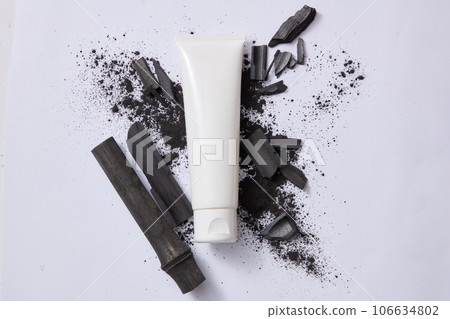 A plastic tube of cream or facial cleanser with bamboo charcoal and powder on gray background. Facial cleanser made from bamboo charcoal helps remove impurities & deeply cleans the skin. Top view 106634802