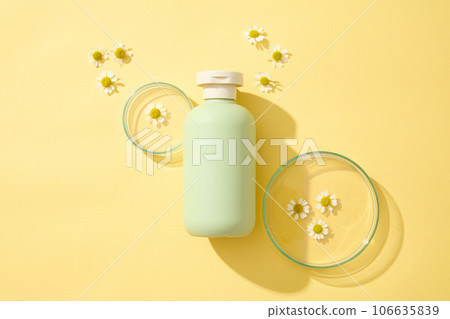 Top view of green plastic bottles of cream or lotion and with chamomilla flowers displayed on yellow background with petri dish. Blank label for design. Mockup scene for advertising Top view of green plastic bottles of cream or lotion and with chamomilla flowers displayed on yellow background with petri dish. Blank label for design. Mockup scene for advertising 106635839