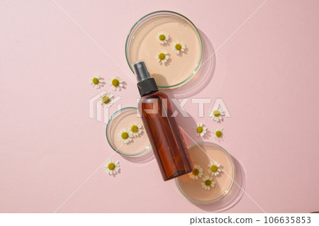 A amber spray bottle unlabeled placed on petri dishes with chamomilla flowers and essence on a pink background. Minimal art background for cosmetics, business branding and product presentation A amber spray bottle unlabeled placed on petri dishes with chamomilla flowers and essence on a pink background. Minimal art background for cosmetics, business branding and product presentation 106635853