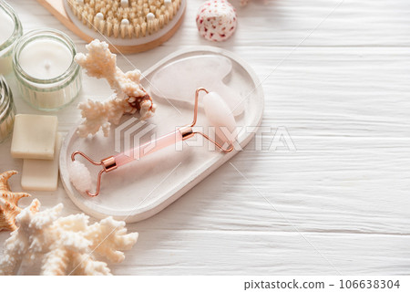 Spa beauty products for body and face home skin care on white wooden background. white towel, bar of soap, jar of cream, pink face roller, wooden brush, and starfish. Self-Care and Beauty concept 106638304