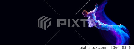 Freedom. Young guy in stylish clothes falling down against black studio background in neon with mixed lights effect 106638366