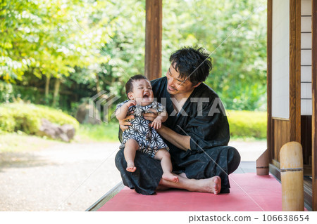 A 9-month-old baby in a jinbei who smiles when he is held by his father in a yukata on the porch of a Japanese house with lots of greenery in summer A 9-month-old baby in a jinbei who smiles when he is held by his father in a yukata on the porch of a Japanese house with lots of greenery in summer 106638654