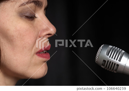 Portrait of a singing woman with a microphone in her hands on a black background Portrait of a singing woman with a microphone in her hands on a black background 106640239